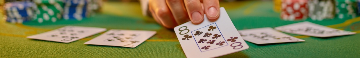A hand holds a poker card over a green poker table.