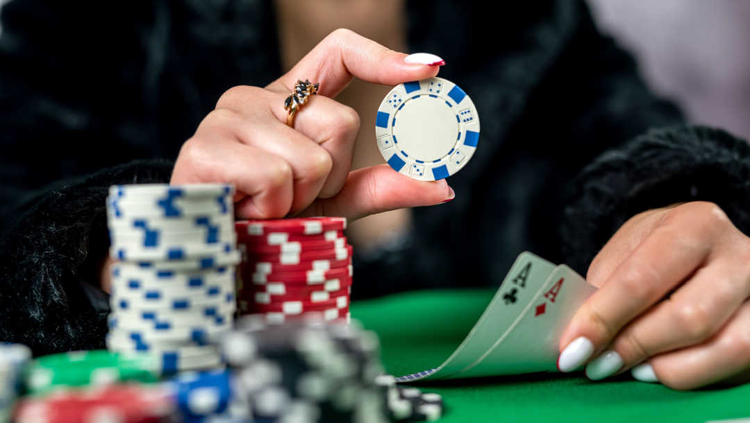  A person with manicured nails holds up a poker chip and two aces.
