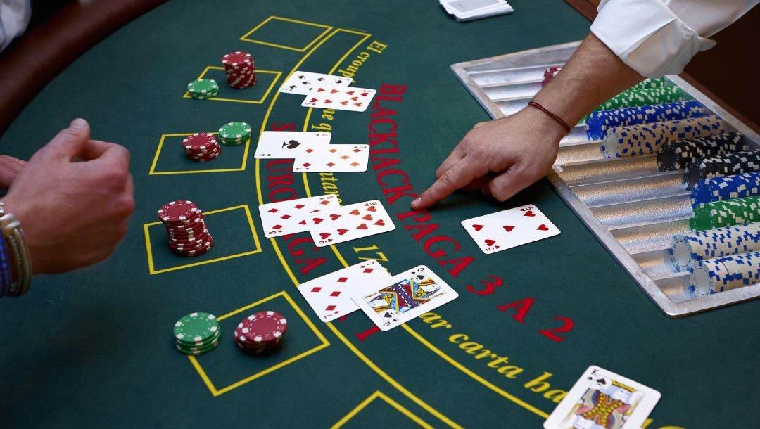 The croupier points to the cards that are laid out on the blackjack table, there is a player sitting opposite him 