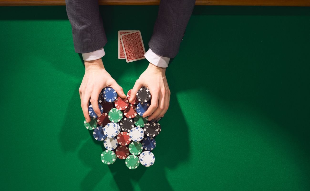  top shot of a man’s hands pushing all his poker chips forward on a green felt poker surface with two playing cards in front of him 
