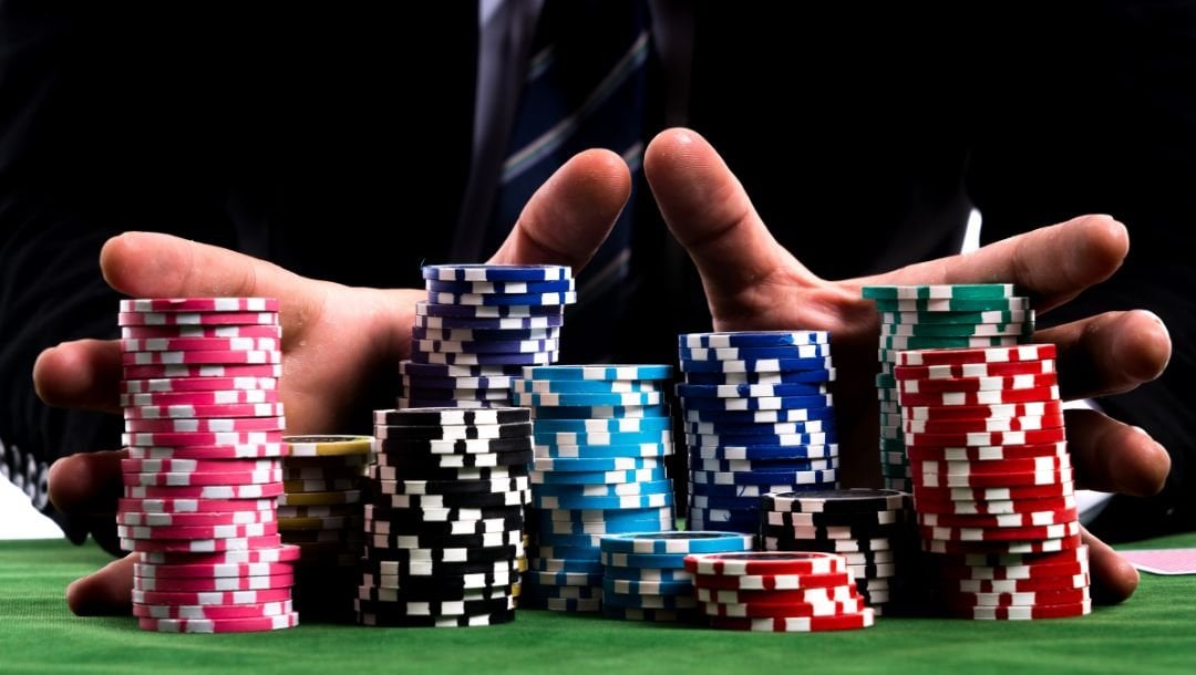 A person in a suit pushes stacks of poker chips forward on a poker table.